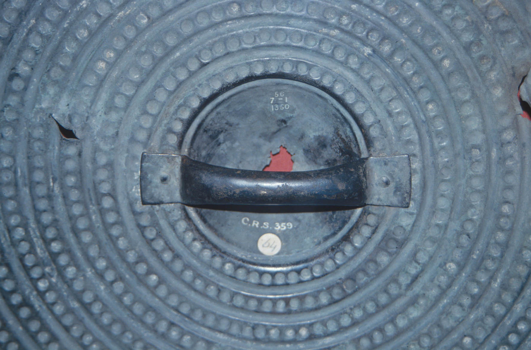 A round shield with raised dot decoration in concentric circles. There is a close up of the hand grip in the centre A round shield with raised dot decoration in concentric circles. There is a close up of the hand grip in the centre