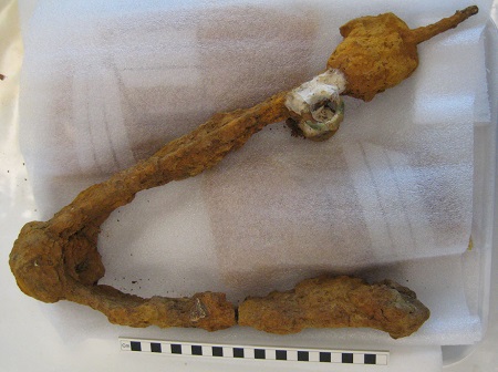 A bent metal object lying on top of soft packaging covered in corrosion
