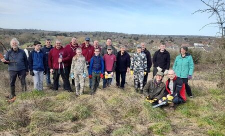 Group of volunteers stood and sat together in scrubby grassland with view of opposite woodland valley behind