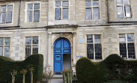 Facade of building with arched doorway with ornate surround and blue door (lower right hand section open)