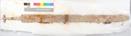 Blade and hilt of sword looking like covered in stone sat on white tissue paper