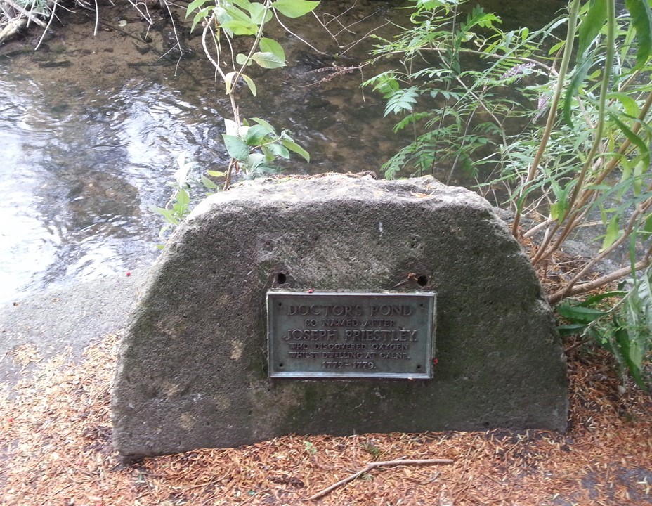 Semi-circular stone with a plaque next to a pond. The plaque reads 