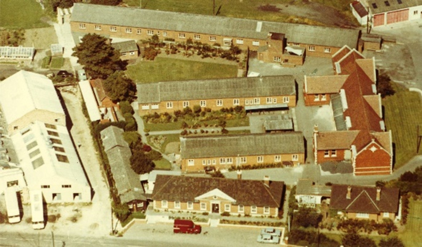 Aerial photograph showing new headquarters at the bottom with red van parked in front and surrounded by other brick buildings and industrial unit to the left.