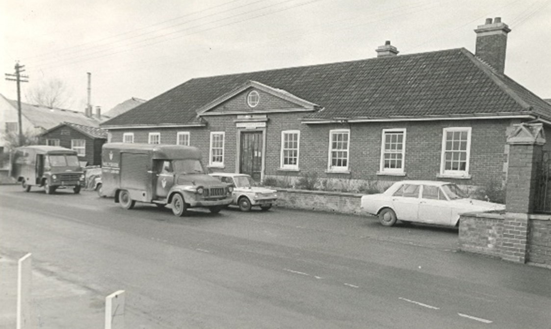 Library van and cars parked outside the long single storey library headquarters building.