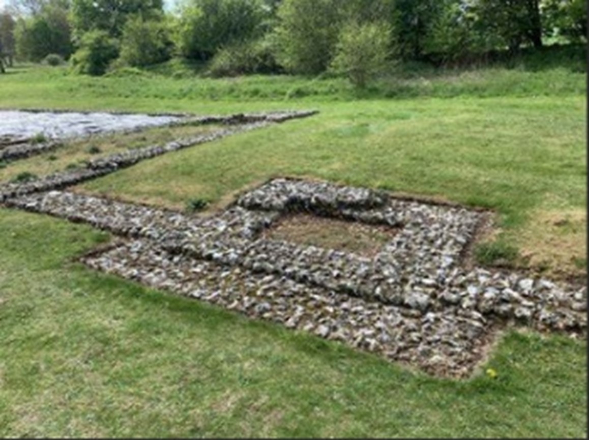 View of grass with rectangular foundations of walls and rooms.
