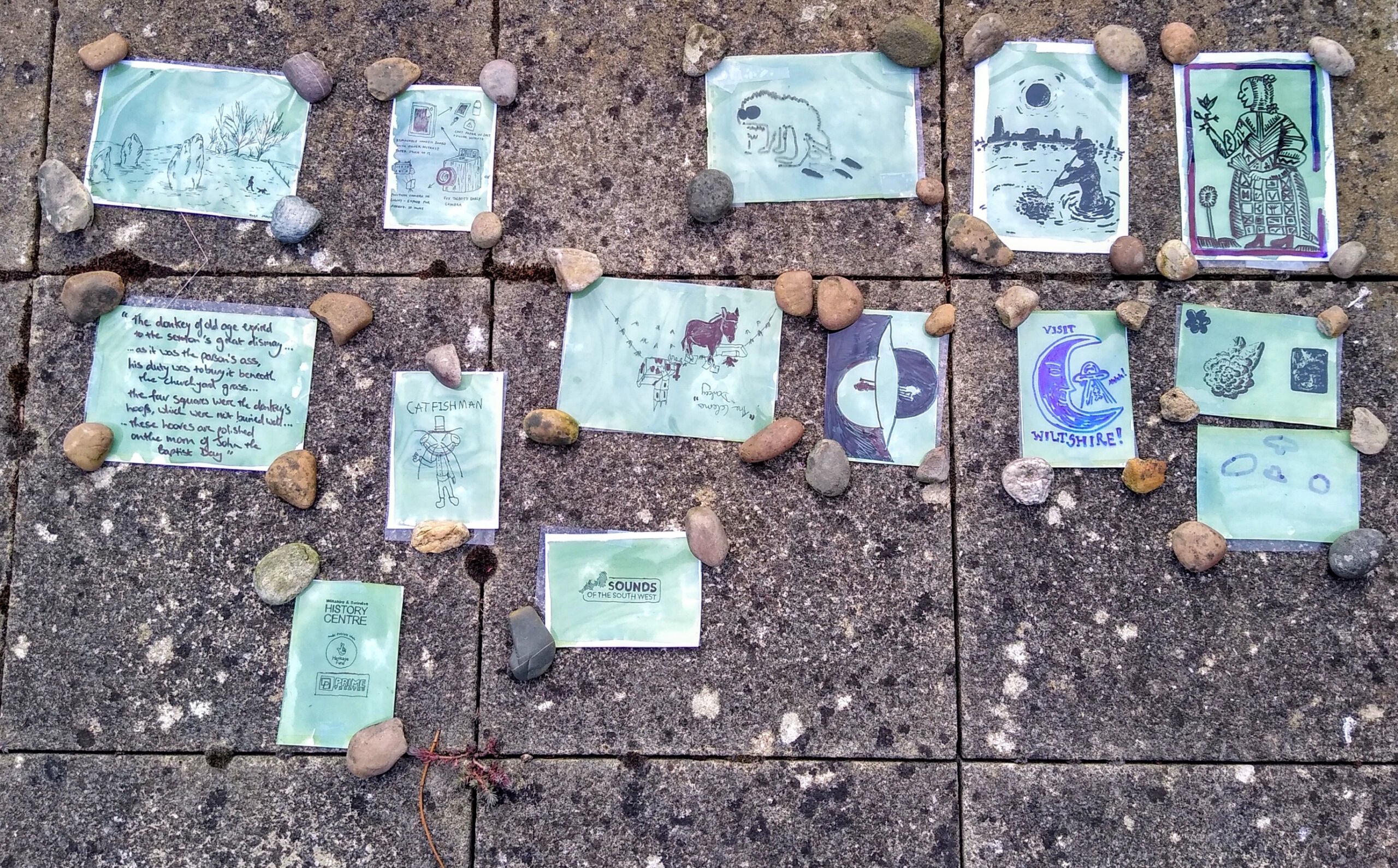 Array of recently developed prints laid out on paving stones held down by stones in their corners