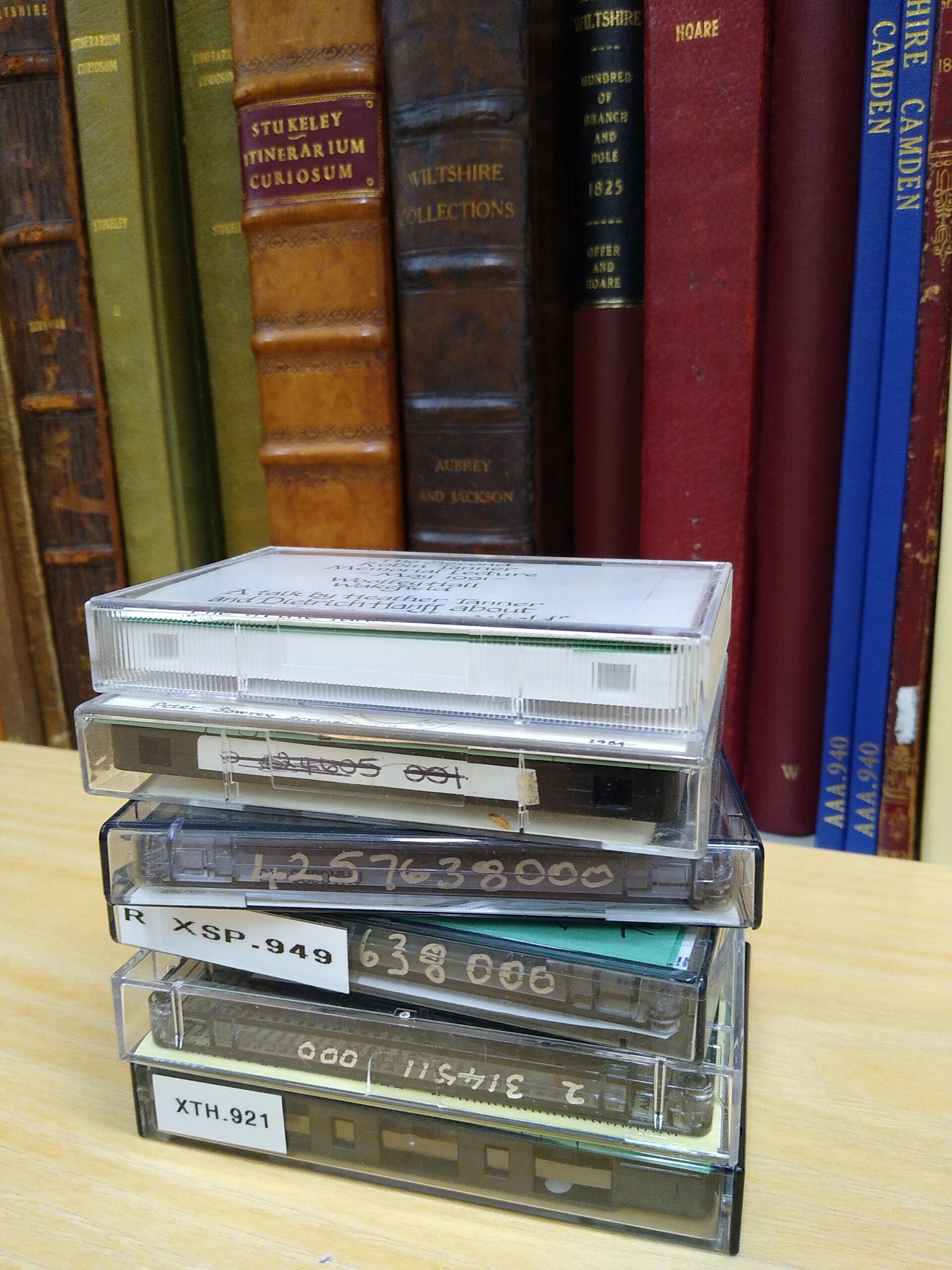A stack of cassette tapes in their cases on a table in front of leather-bound books