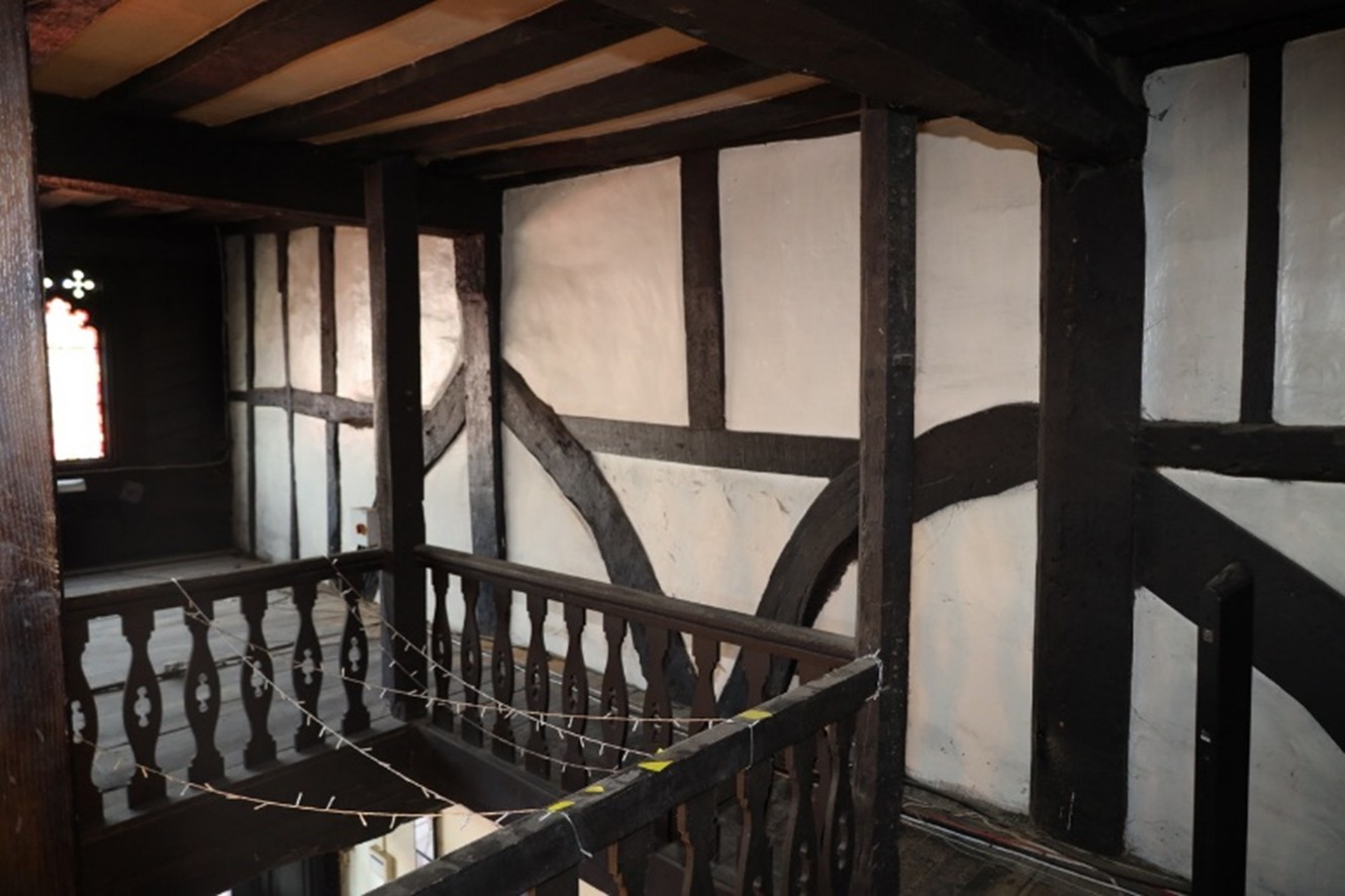 Timber balustrade and wall panelling with glimpse of window tracery on far left.