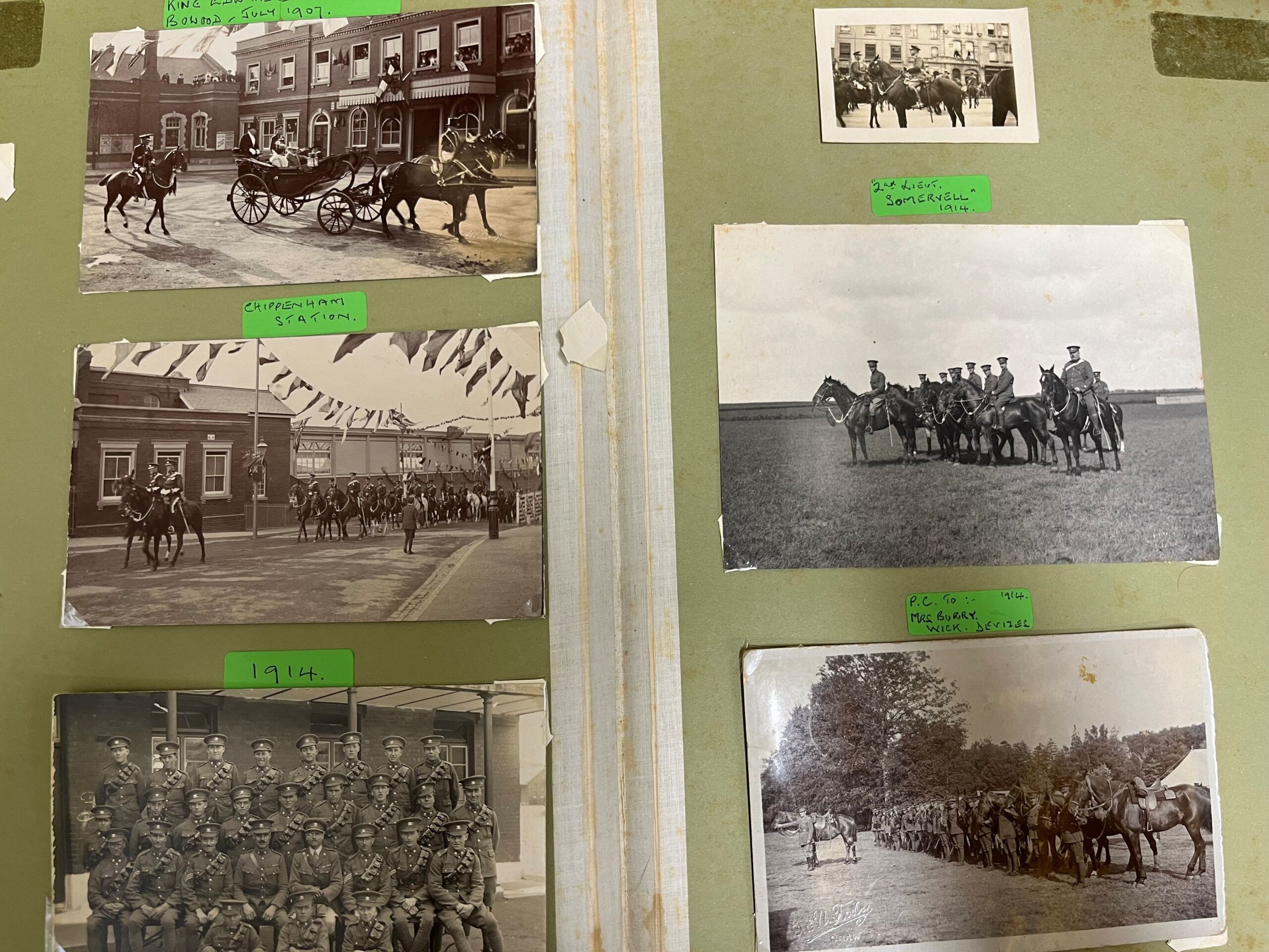 Green paper background to photograph album with six black and white photos showing uniformed soldiers (group photo, two with lines of soldiers with horses on training grounds, and another with horse and carriage annotated with King Edward, Bowood, July 1907. Other photos annotated with date of 1914.