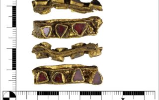 Scale image showing four views of ornate gold ring with irregular triangular red gems inserted.